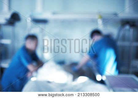 Two male medical workers working with critical condition patient in the intensive care unit unfocused background.