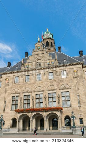 ROTTERDAM HOLLAND- AUGUST 23 2017; Two people one standing the other walking by on pavement below steps of Stadhuis or Town Hall with bell tower and statue of golden peace angel a National Monument and one of few old buildings left on the city.