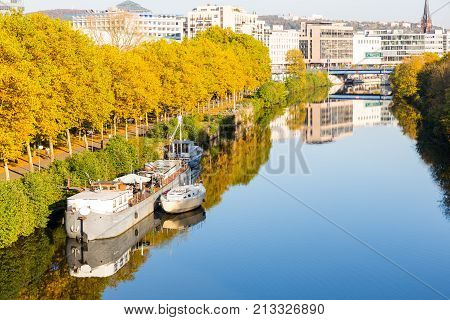 small and big boats on river near promenade leading to city center with shopping malls and church reflection in river autumn colors beautiful day light saarbrucken saarland germany