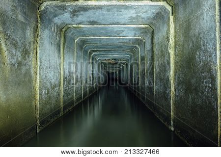 Dark and creepy flooded underground sewer concrete tunnel. Industrial wastewater and urban sewage flowing throw the tunnel.
