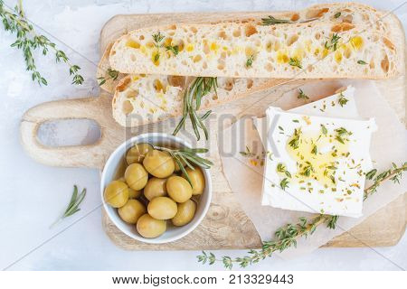 Green olives feta cheese and fresh ciabata on a wooden board light background top view.
