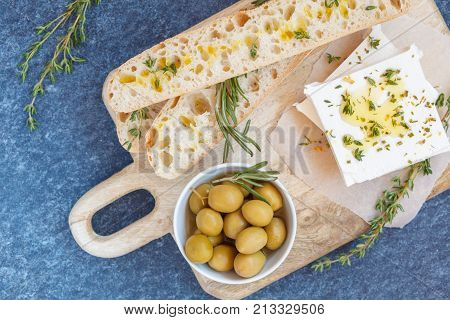 Green olives feta cheese and fresh ciabata on a wooden board dark background top view.