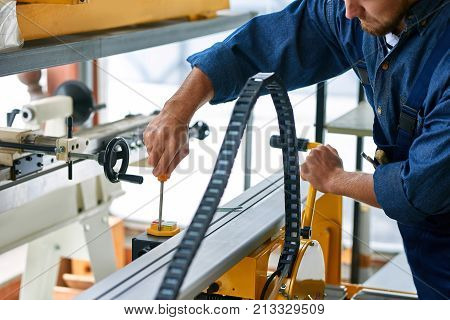 Closeup of workman  fixing machine unit tying screws with screwdriver at modern factory, copy space
