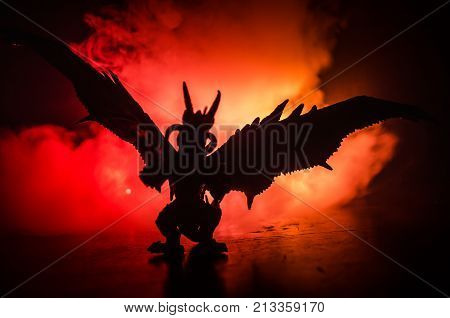 Silhouette Of Fire Breathing Dragon With Big Wings On A Dark Orange Background. Empty Space