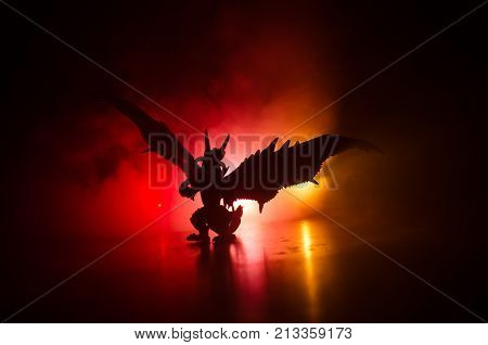 Silhouette Of Fire Breathing Dragon With Big Wings On A Dark Orange Background. Empty Space