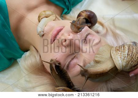 Skin treatment and regeneration with snails. Young blonde with a lot of snails on her face in beauty salon. Girl in spa salon receiving snails therapy for skin cleaning and rejuvenation.