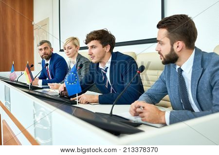 Portrait of several business people sitting in row participating in political debate during press conference answering media questions