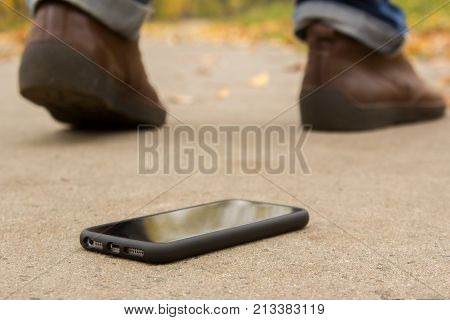 The man lost the phone. Men leave and only the legs and shoes are not in focus and the phone on the ground