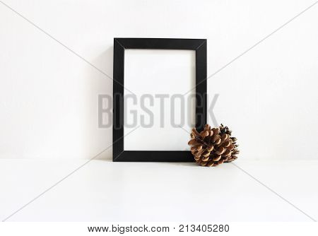 Black vertical blank wooden frame mockup with pine cones lying on the white table. Poster product design. Styled stock feminine photography. Home decor, Christmas winter concept.