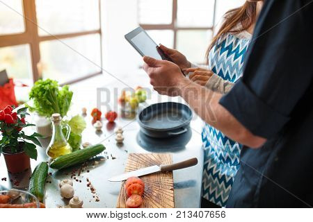 A beautiful young couple uses a digital tablet to select a dish for dinner. The concept of cooking.