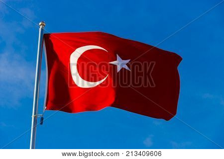 Flag of Turkey on flagpole waving in the wind against the blue sky close up