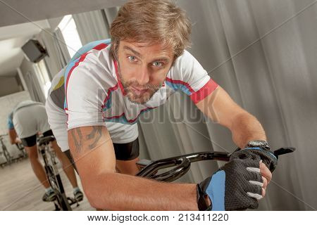 Young handsome and fitt man is looking to camera and posing in a cycling gym.