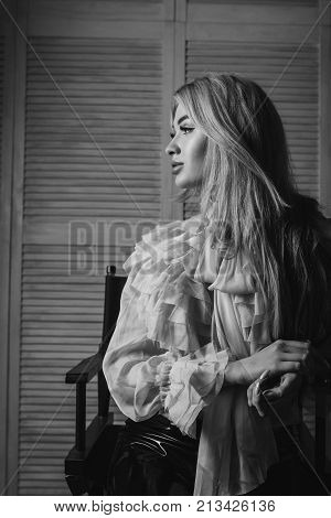 Excited Blonde Sits On A Chair In A Lacy Blouse And Looks At The Light. Long Legs In Latex Pants. Gl