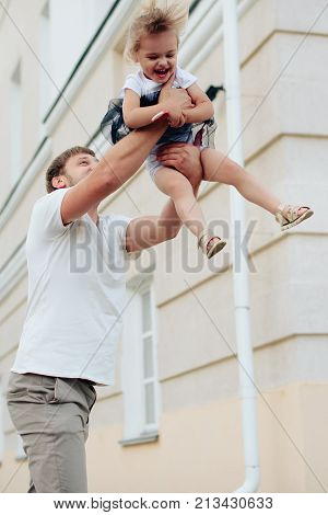 father holds little daughter in her arms on the background of the building 1