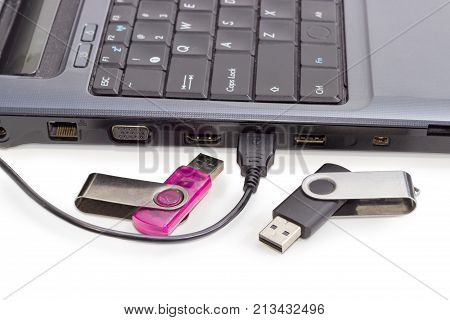 USB cable connected to laptop and two different USB flash drives beside on a background of a side part of laptop
