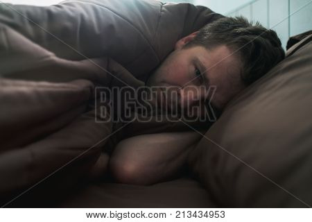 offended caucasian man lie on bed and cover himself with blanket. He is about to cry. Negative human emotion.