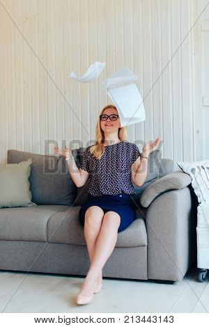 beautiful blond woman with glasses sits on the couch and throws up paper 1