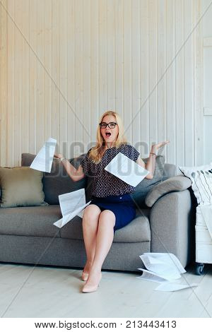 beautiful blond woman with glasses sits on the couch and throws up paper 1
