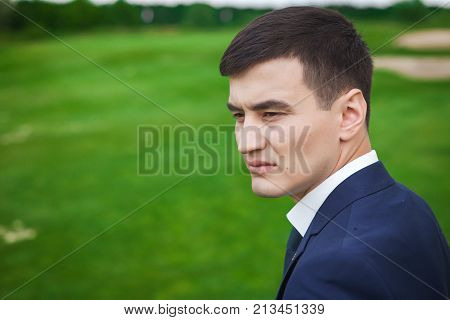 Portrait of handsome, thoughtfull asian groom in a dark blue against the backdrop of green golf field. concept of a strong successful man