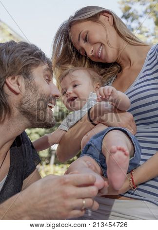 A young beautiful couple are teesing their happy woughing cute baby.