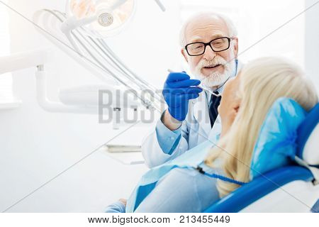 Real professional. Skilled dentist using specific tools and inspecting patients mouth cavity while the patient sitting on the dental chair