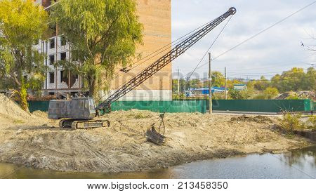 Excavator standing on the shore clears the bottom of the lake from dirt and debris