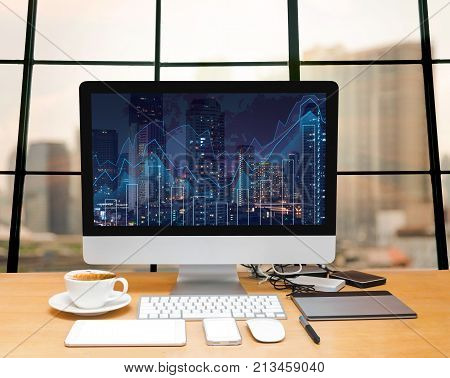 Workspace with computer desktop on the wood table with trading graph at the screen on the blurred photo of cityscape building background