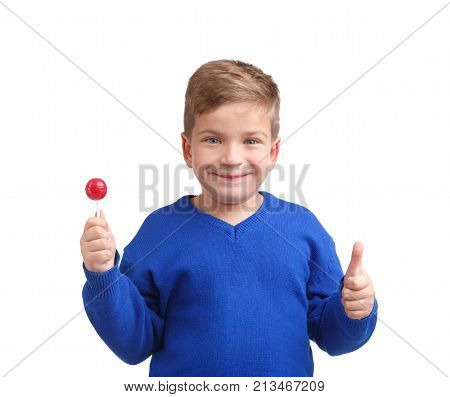 Boy with a smile in a blue sweater with a lollipop in his hand showing a thumb on a white isolated background