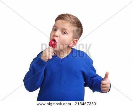 A boy in a blue sweater licks a lollipop and shows a thumb that he is delicious on a white isolated background