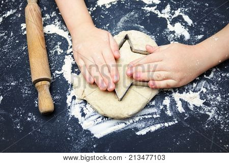 Little child hands with cookie cutter like a star making handmade traditional Christmas cookies. An overhead photo of kid's hands, some flour, wheat dough, cookie cutter and rolling pin on the table