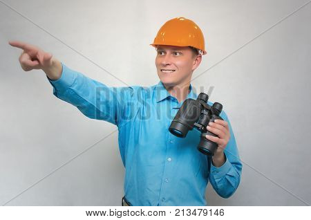 Engineer holding binoculars in one hand and showing ahead with his index finger isolated. Geodesist explore construction site.