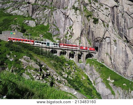 ANDERMATT, SWITZERLAND EUROPE on JULY 2017: Express St. Gotthard train on Teufelsbruecke, Devil's railway bridge and tunnel, swiss Alps, alpine rocky mountains landscape scenery in warm summer day.