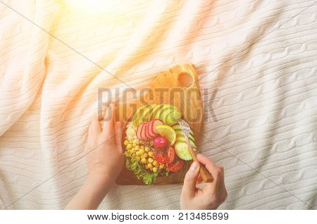 Girl in white jeans holds in hands fork, vegan breakfast meal in bowl with avocado, quinoa, cucumber, radish, salad, lemon, cherry tomatoes, chickpea, chia seeds. Top view, copy space. Clean eating.