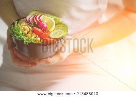 Girl in white jeans holds in hands fork, vegan breakfast meal in bowl with avocado, quinoa, cucumber, radish, salad, lemon, cherry tomatoes, chickpea, chia seeds. Top view, copy space. Clean eating.
