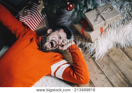 Sleepy bearded guy has just woken up after long sleep. He is stretching and yawning. This man had a good time celebrating Christmas with his friends and family last night. But now it's time to wake up and do some things. Close up. Cut view