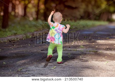 The first independent steps of the child. A cute little girl is walking along the road on a summer sunny day.