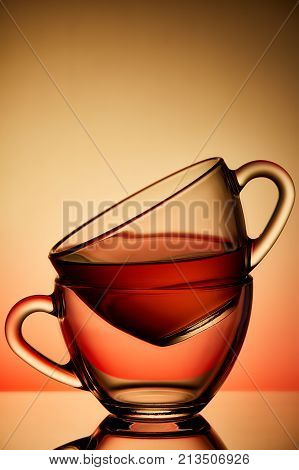 Two cups and saucers of glass. Tea is poured into the top Cup. Helium filter gives a beautiful light. Studio photos using the backlight. The reflection on the black table. The background is orange-red.