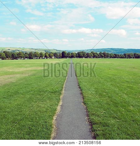 long straight footpath stratching to the distance in a park with grass lawn and trees in the background in halifax yorkshire