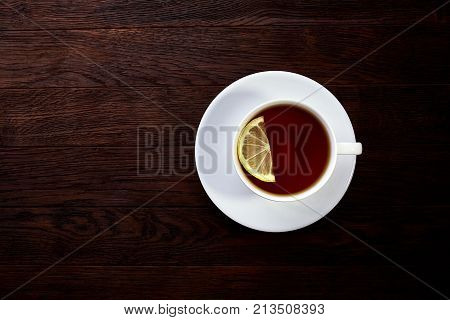 Tea with lemon in white cup, cinnamon sticks, knitted woolen scarf on a wooden table