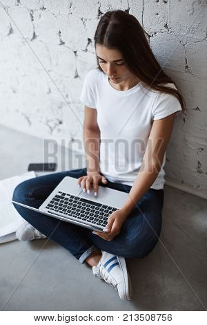 Young female architect using laptop computer to create blueprints of new building for her mid term exam.