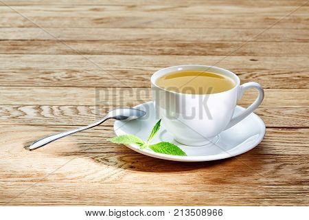 Tea with lemon in white cup, cinnamon sticks, knitted woolen scarf on a wooden table