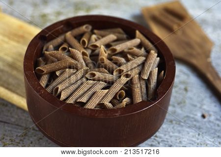 closeup of a wooden bowl full of uncooked buckwheat penne rigate on a gray rustic wooden table