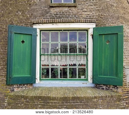 house window with wooden green shutters and lace curtain valance