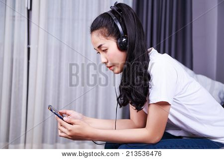 Woman Listening To Music In Headphones With Moblie On Sofa At Home