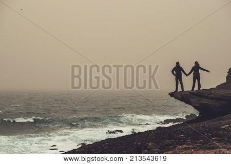 Couple standing on a cliff in a storm.