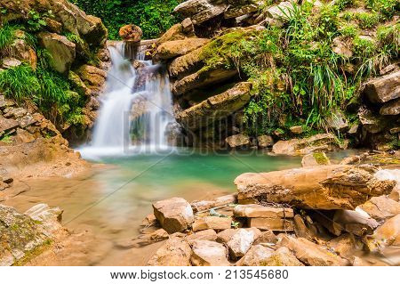 Waterfall with boulders and small lake in the ravine Chudo-Krasotka in summer day Sochi Russia