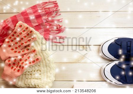 Winter clothes ;blue sneaker ,white wool hat,pink wool gloves and red scarf on white wood board background  with snow.Winter season concept
