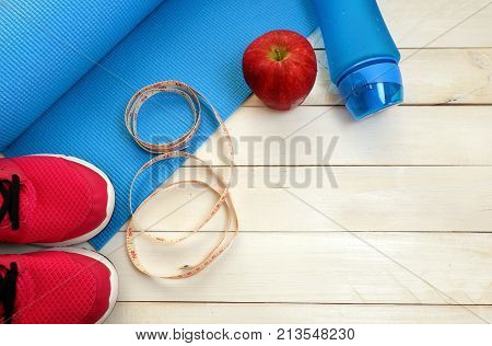 Fitness concept,exercise for losing weight with sport set,sport shoes,mat,drinking bottle ,fresh fruit on white wood floor. Top view for copy space