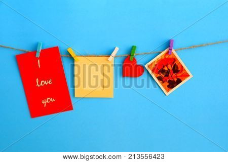 Clothespin with frame card ,heart,bow and love card hanging on rope on blue background