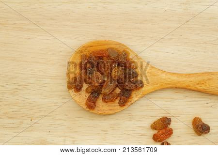 Dried raisins in wooden spoon / spatula on wooden background.